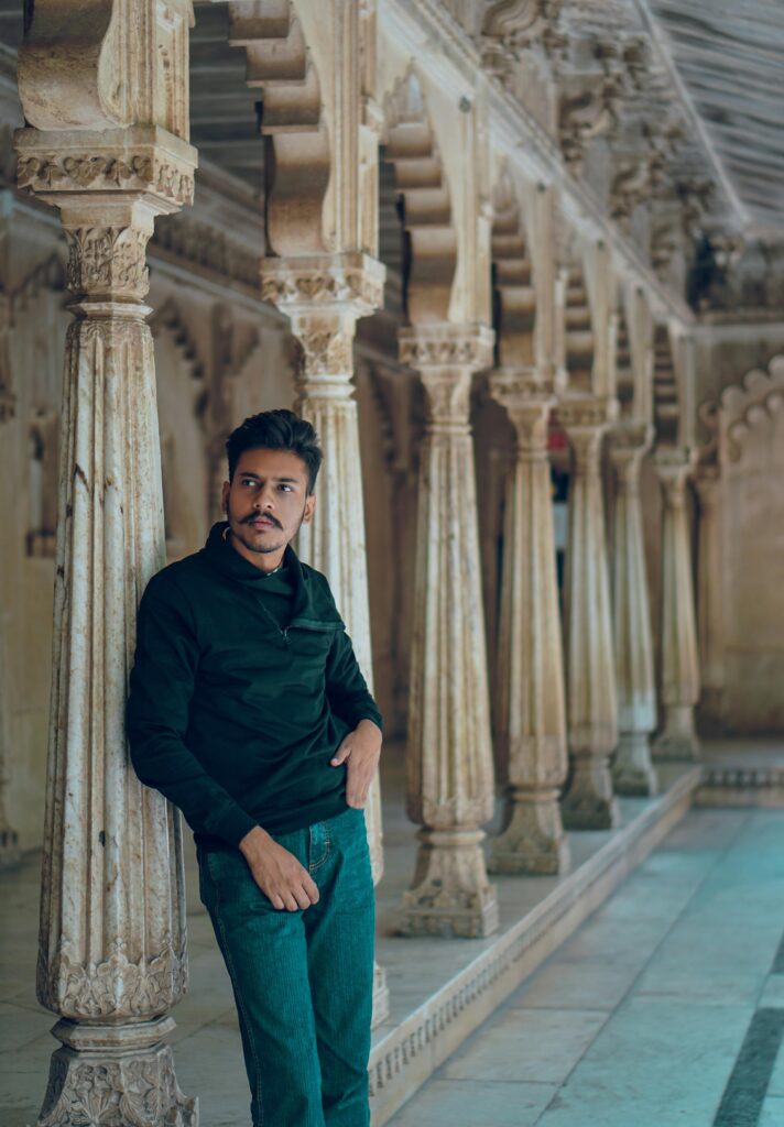 A South Asian man poses against ornate stone columns in an Indian palace.